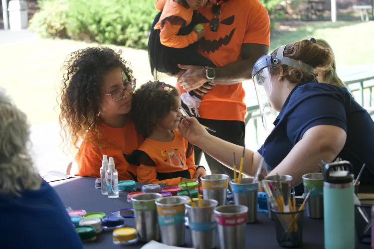 Woman holding child while child's face is painted