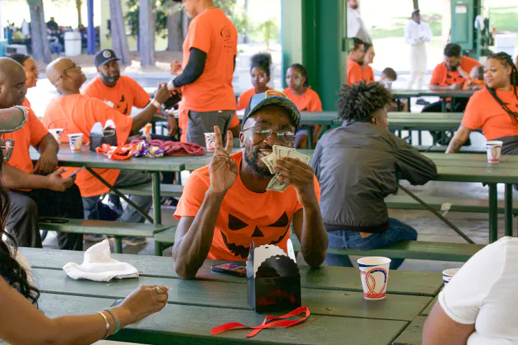 Man making peace sign, holding money, smiling at outdoor banquet